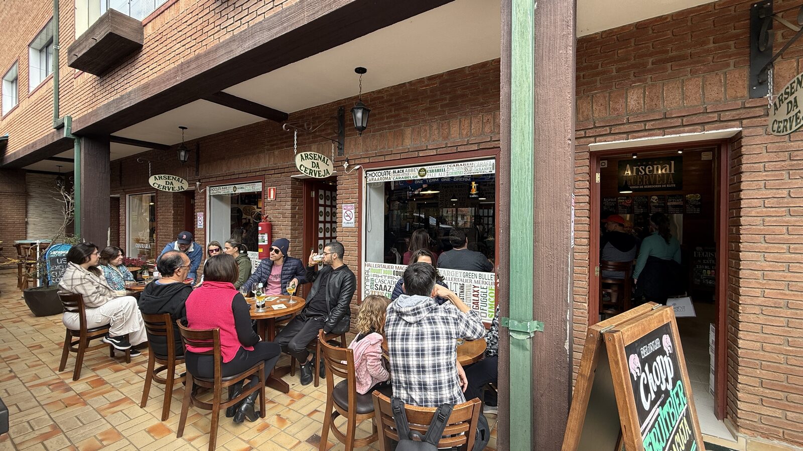 Fachada do Arsenal da Cerveja na Galeria Suíça, em Monte Verde, com clientes nas mesas da calçada