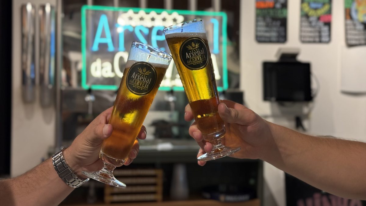 Brinde de duas taças de chopp em frente ao letreiro neon do Arsenal da Cerveja