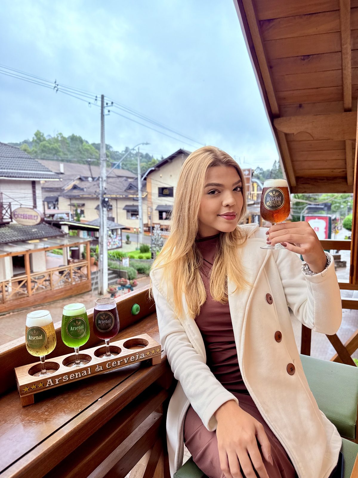 Cliente na varanda do Arsenal com a régua de degustação e a vila de Monte Verde ao fundo