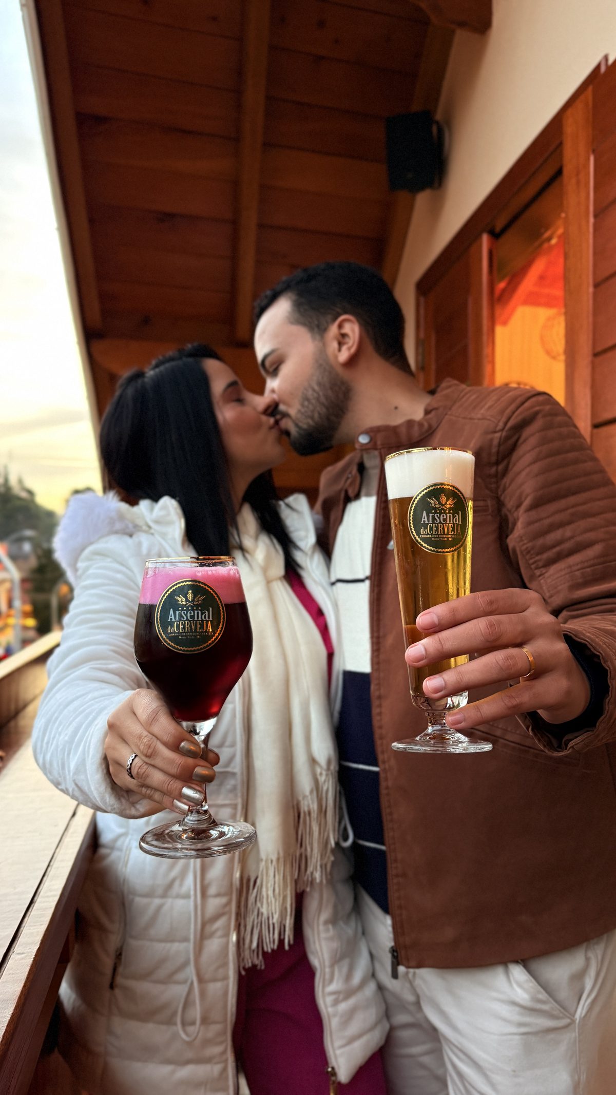 Casal se beijando com taças da régua de degustação na varanda do Arsenal