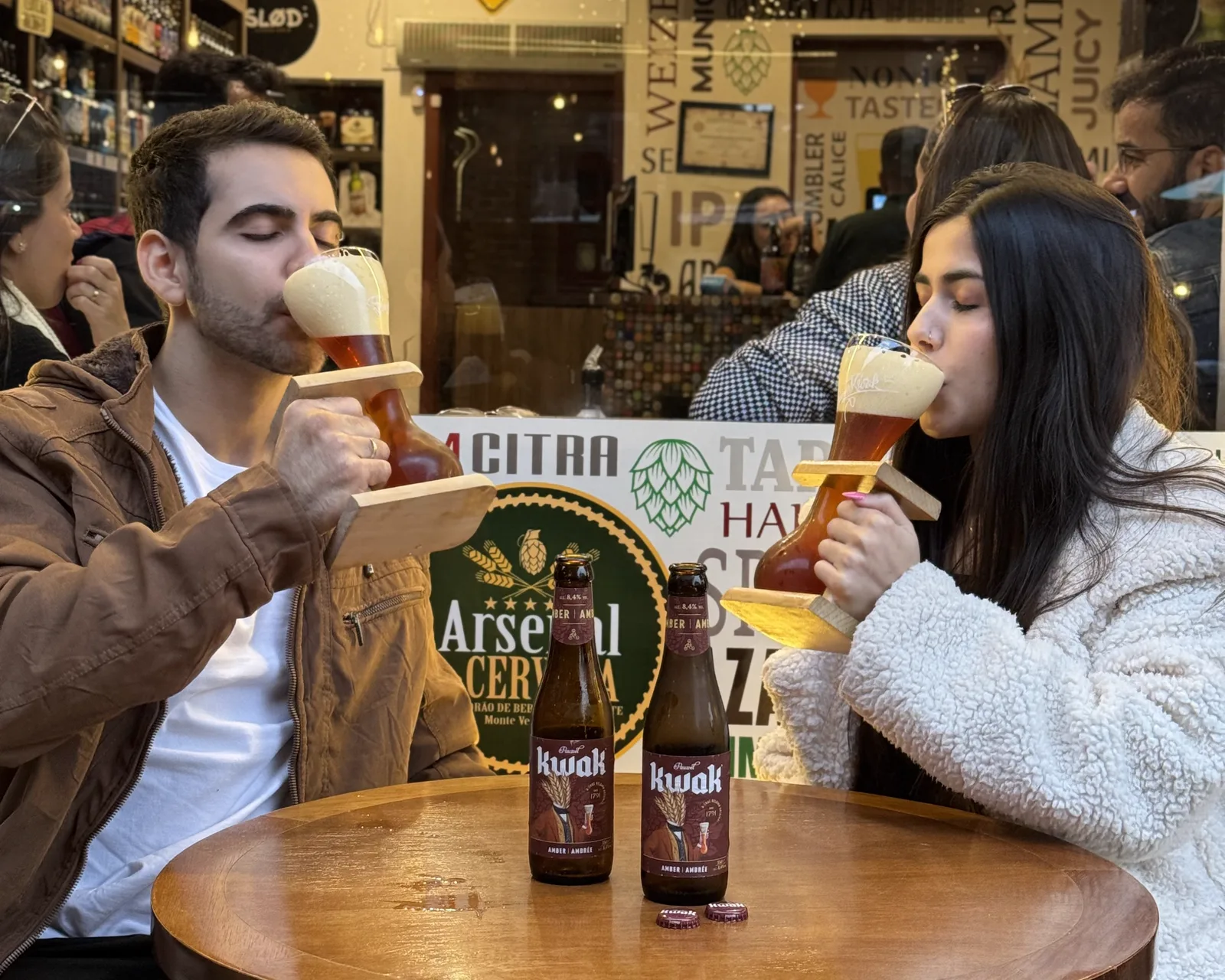 Casal degustando cervejas especiais em taças Kwak com suporte de madeira no Arsenal da Cerveja, em Monte Verde